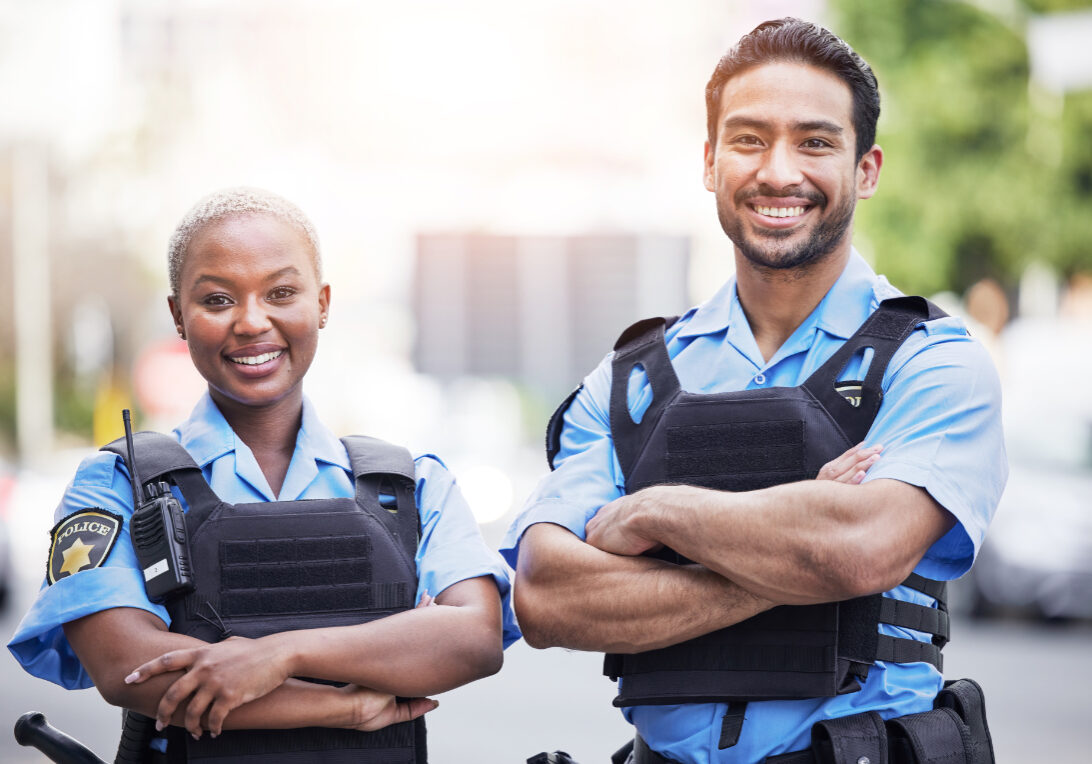 Happy, portrait and police with arms crossed in the city for security, safety and justice on the street. Team, pride and a black woman and a man with confidence working in urban crime together.
