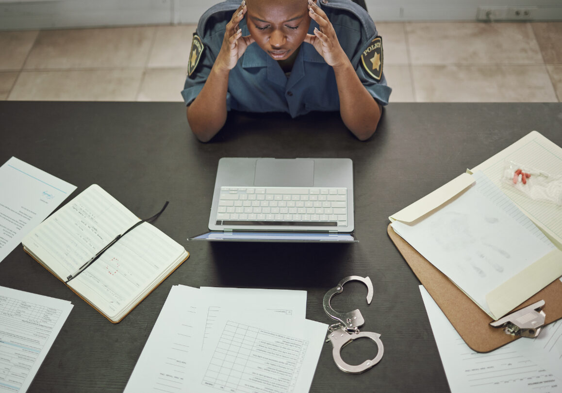 Police, woman and working with stress at desk with documents, paperwork or frustrated with headache from working on computer case, report. Security, officer and tired from work in office or station.